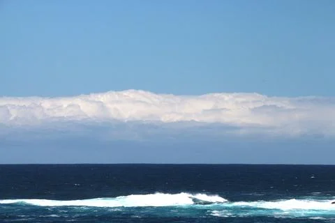Ocean waves rolling gently under a bright blue sky with clouds in the distanc Stock Photos