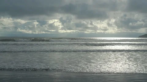 Ocean waves rolling onto a quiet beach beneath dramatic storm clouds with Stock Footage 341755202