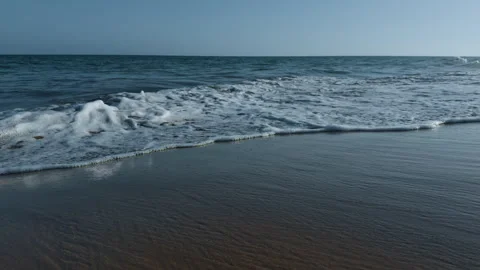 Ocean waves rolling onto a sandy beach under a clear blue sky. Peaceful coastal Stock Footage 337865055