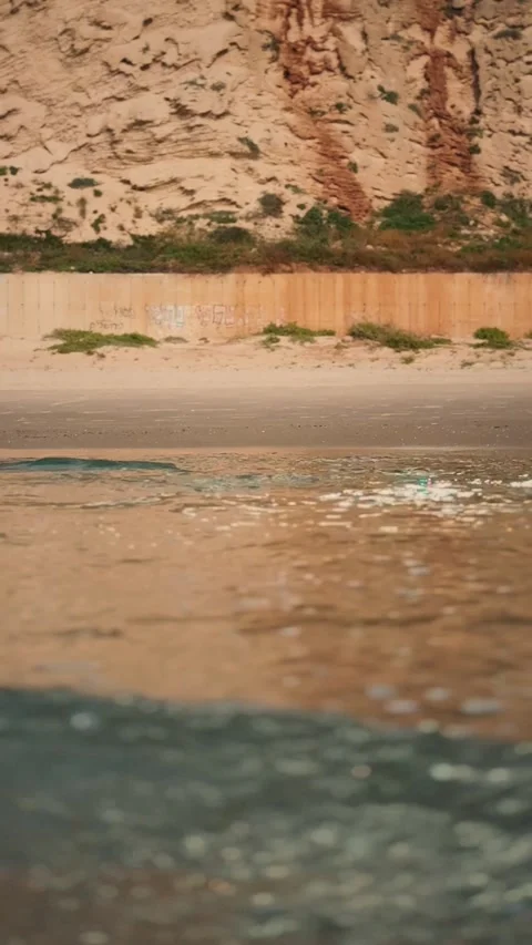 Ocean Waves Rolling onto Sandy Beach beneath Rocky Cliff Stock Footage 341527409