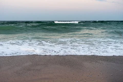 Ocean waves rolling onto sandy beach with foam at sunset Stock Photos