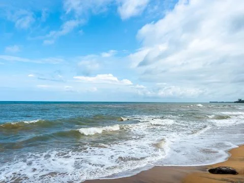 Ocean waves rolling onto a sandy beach under a dramatic blue sky with cloud.. Stock Photos