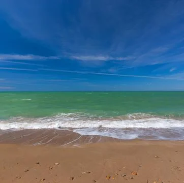 Ocean Waves Rolling onto a Sandy Beach Under a Dramatic Blue Sky 스톡 사진