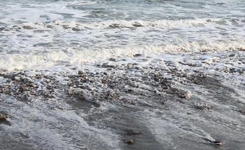Ocean waves rolling toward a wet pebble beach Stock Photos