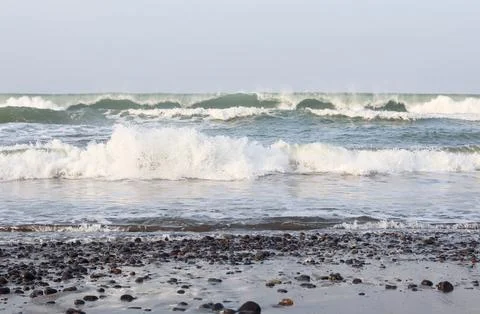 Ocean waves rolling toward a wet pebble beach Stock Photos