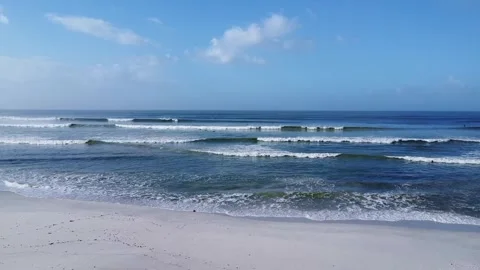 Ocean waves rolling towards the sandy beach under a partly cloudy blue sky on a Stock Footage 308963136