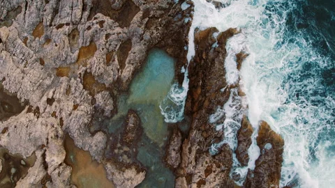 Ocean waves rush through jagged tide pools among colourful sea-worn rock layers Video stock 319871694