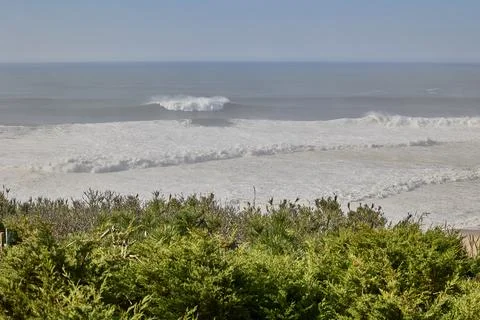 Ocean waves seen from coastal cliffs with green shrubs Stock Photos