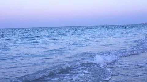 Ocean waves with soft white crests meet sandy shore under sky tinged with pre Stock Photos