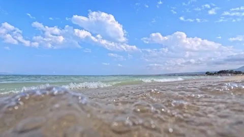 Ocean waves softly touch sandy beach beneath scattered white clouds Stock Footage 341775785