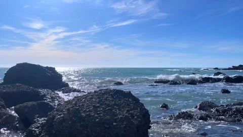 Ocean waves sparkle on rocks under bright blue summer sky Stock Footage 310243592