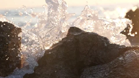 Ocean waves splash dramatically over dark rocks in warm sunlight Stock Footage 337410578