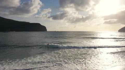 Ocean waves at sunset with a surfer and a cliff in the background Vidéo 195333019