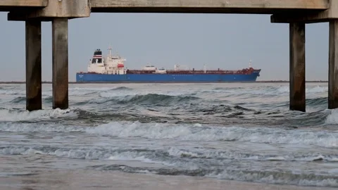 Ocean waves under a pier at dusk as a distant ship goes out to sea. Stock Footage 236951725