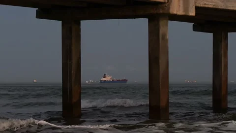 Ocean waves under a pier at dusk as a distant ship goes out to sea. Stock Footage 236965419