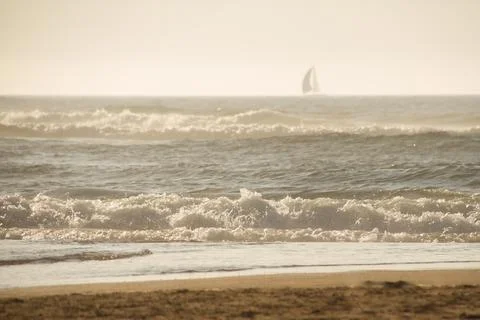 Ocean waves under the sunset with shape of sailboat on the horizon Stock Photos