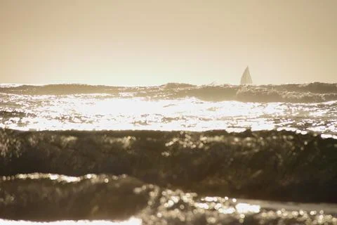 Ocean waves under the sunset with shape of sailboat on the horison Stock Photos