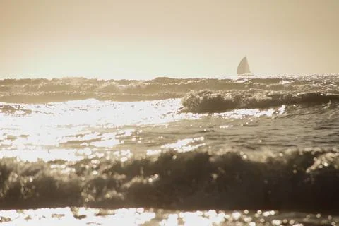 Ocean waves under the sunset with shape of sailboat on the horison Stock Photos