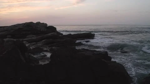 Ocean waves washing over dark rocks at dusk. Aerial drone low flight Stock Footage 309627048