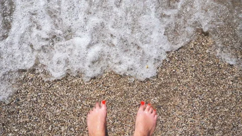 Ocean waves washing over slim female feet. Woman standing on seashore Stock Footage 135250076