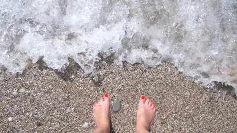 Ocean waves washing over slim female feet. Woman standing on pebble beach Stock Footage 292766494