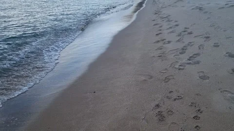 Ocean waves washing sandy beach with footprints during peaceful sunset evening Stock Footage 320044681