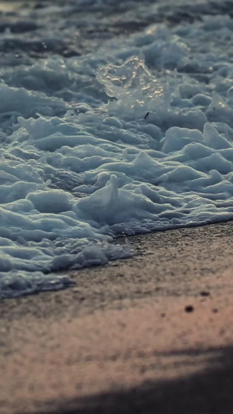 Ocean waves washing onto sandy beach during golden hour, water movement creating Stock Footage 335764162