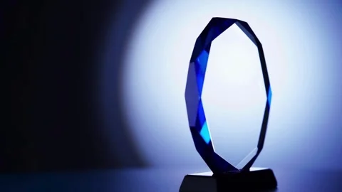 An octagonal crystal trophy rotates under a blue spotlight Stock-Footage 333810726