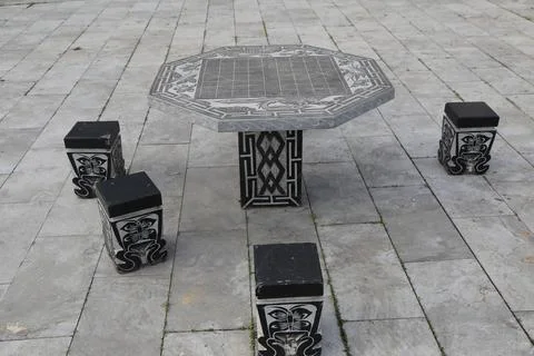 Octagonal stone game table and four square stools on an empty paved courtyard Stock Photos
