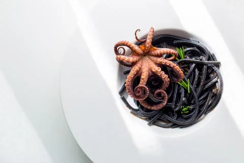 Octopus with black pasta in white plate. Stock Photos