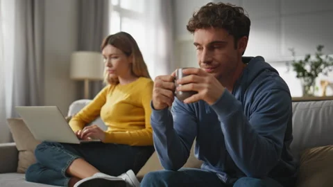 Offended couple ignoring each other at sofa. Bored man drinking coffee cup Vídeo Stock 264931514