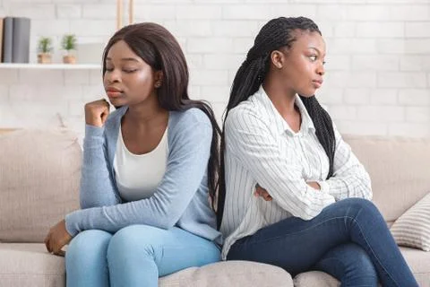 Offended girlfriends sitting back to back, ignoring each other after quarrel Stock Photos