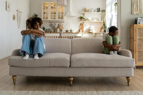 Offended mom and son sit on opposite sides of couch pout at each other ignore Stock Photos