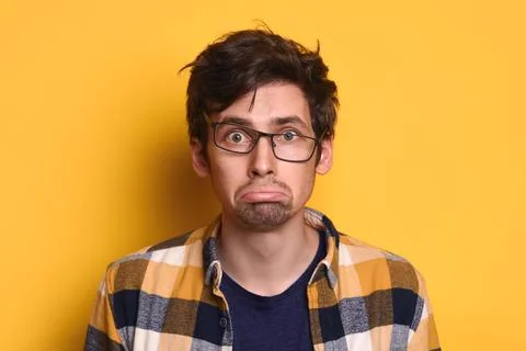 Offended young guy looking at camera isolated on yellow studio wall Stock Photos