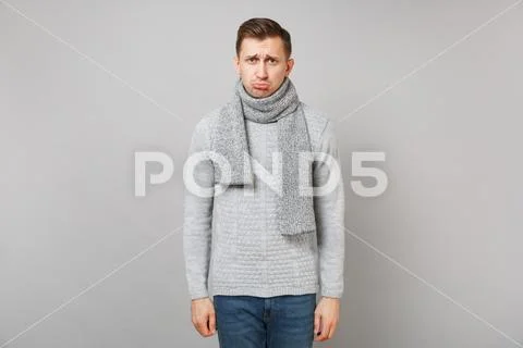 Offended young man in gray sweater, scarf pouting lips isolated on grey wall Stock Photos