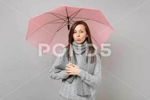 Offended young woman in gray sweater, scarf pouting lips, holding pink umbrella Stock Photos