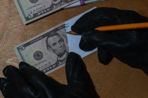 The offender forges a five-dollar bill. The hands are put on gloves to hide the Stock Photos