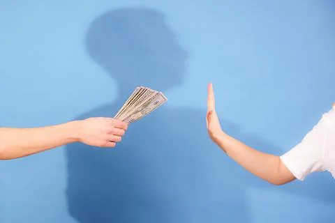 Offering cash while a person refuses with their hand raised against a blue .. Stock Photos