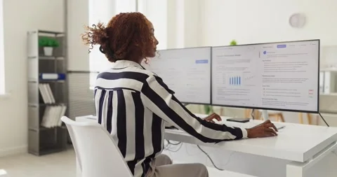 Office analyst using dual monitors for financial dashboard analytics and support Stock Footage 336003784