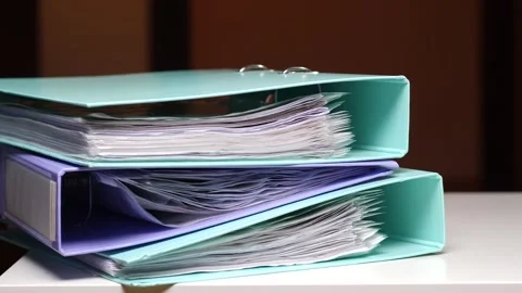 Office binders, full of paperwork, documents, and files, are stacked on a desk Stock Footage 347238616