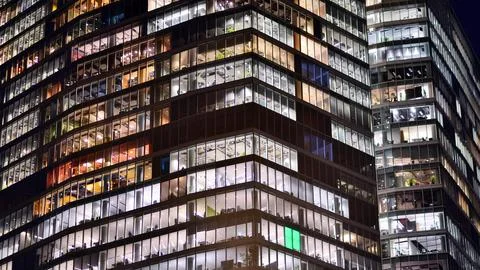 Office building in the evening with lightened workspaces. Stock Photos
