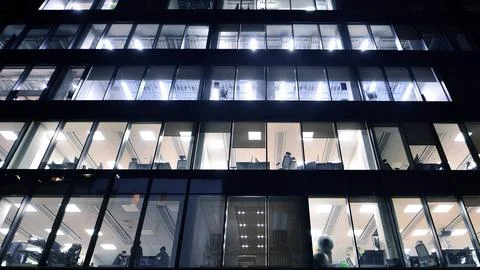 Office building in the evening with lightened workspaces. Stock Photos