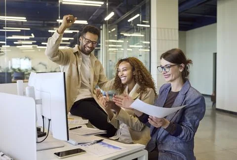 Office colleagues cheering at computer after successful project completion Stock Photos
