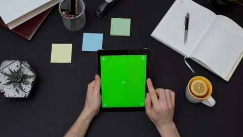 Office desk and tablet computer with green screen and male scrolling on it. Stock Footage 87571027