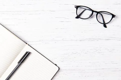 Office desk with empty notepad, pen and glasses, wooden background, top view Stock Photos