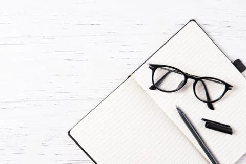 Office desk with empty notepad, pen and glasses, wooden background, top view Stock Photos