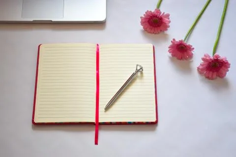 Office desk, open empty notebook with silver pen and three pink flowers Stock Photos