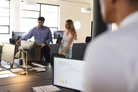 In office, diverse colleagues analyzing data on computer screens, discussing Foto stock