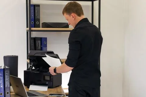 Office employee retrieving printed document from printer in bright workspace Stock Photos
