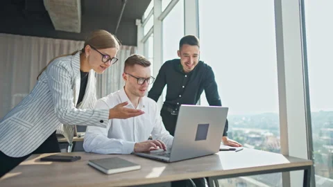 Office employees cooperation at work. Three colleagues looking at laptop discuss Stock Footage 217424740